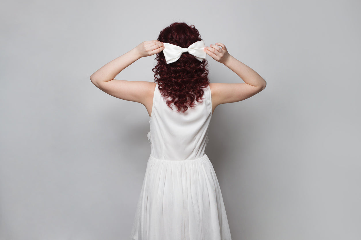 A woman dressed in white showing her curled hair with a bow