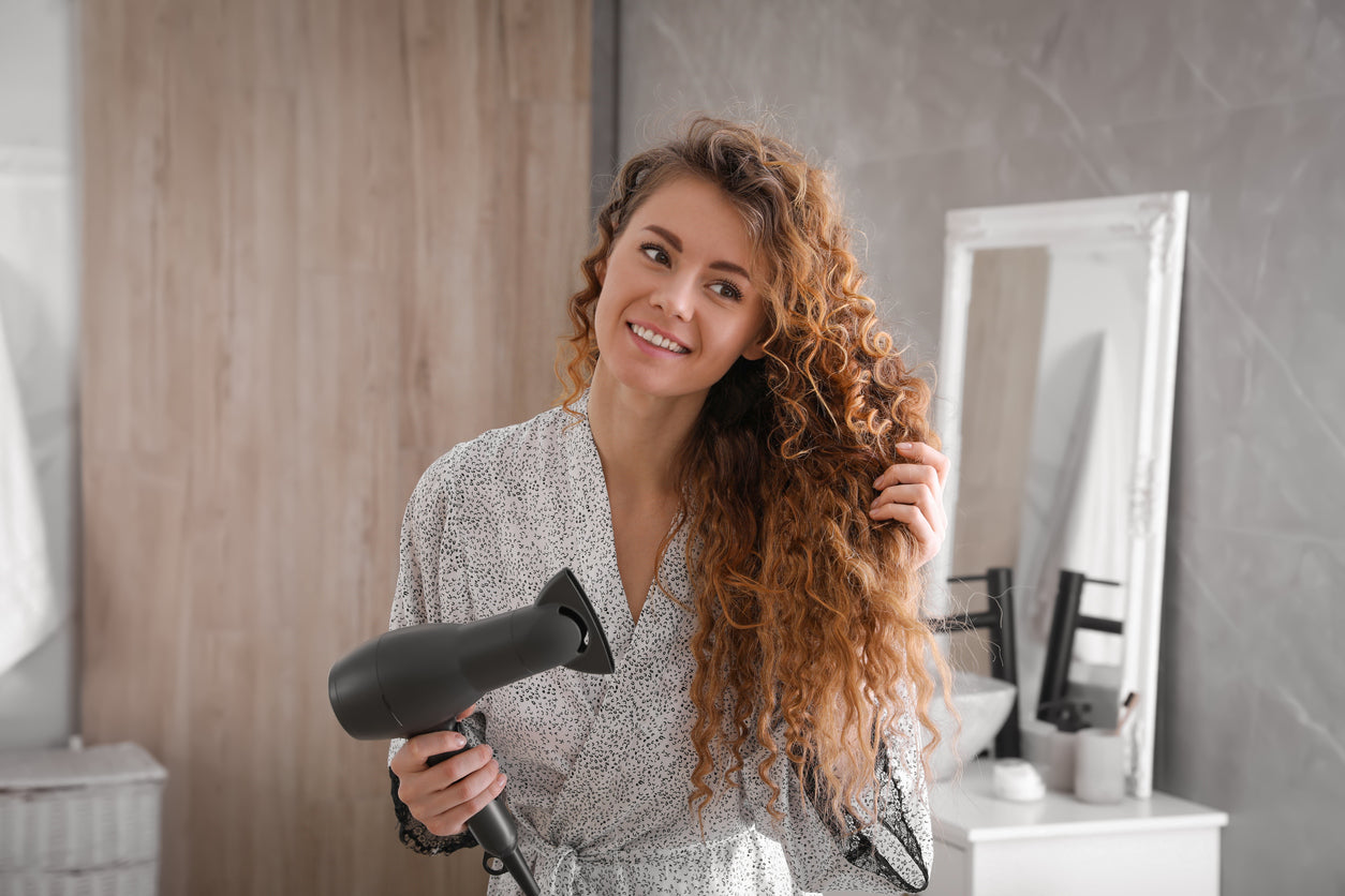  Woman using a blowdryer from the Termix Travel Set to style her long, curly hair.